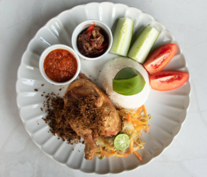 Indonesian rice plate with chicken, sambal, cucumber, tomato, and lime